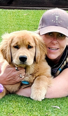 Woman in baseball cap holding a Moxy Goldens puppy on grass